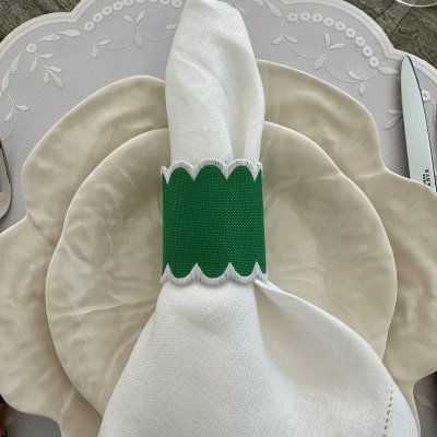 Mesa posta com pratos cerâmicos bege, guardanapo branco com anel verde e suporte cinzento bordado.