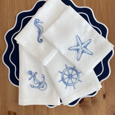 Conjunto de guardanapos brancos com bordados náuticos azuis sobre bases de mesa azul-marinho onduladas