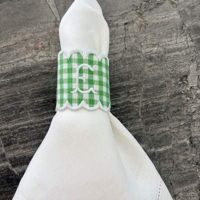 Guardanapo branco com argola verde aos quadrados brancos com bordado branco, sobre pedra cinzenta.