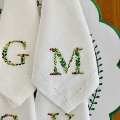 Guardanapos brancos com monogramas bordados em motivos florais coloridos sobre suporte branco com borda verde