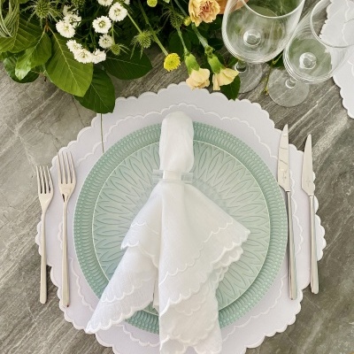 Conjunto de louça com prato verde e branco, guardanapo branco, talheres, copos e arranjo floral