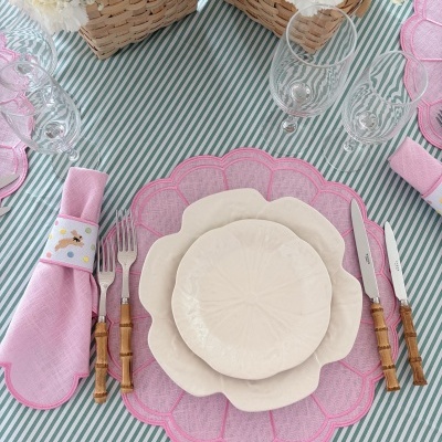 Mesa posta com pratos brancos, sousplat rosa, talheres com cabo de bambu, guardanapo rosa e toalha às riscas verdes e brancas