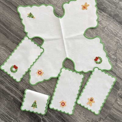 Conjunto de peças de tecido com bordas verdes e motivos natalinos bordados.