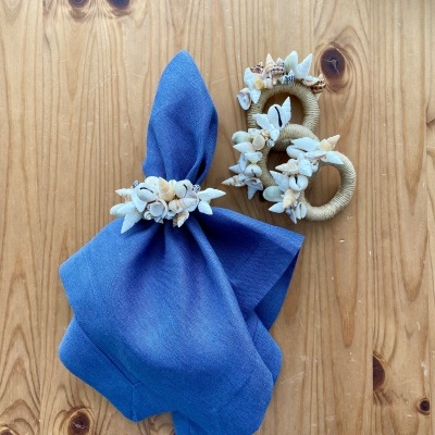 Argolas de guardanapo com conchas e guardanapo azul sobre madeira clara