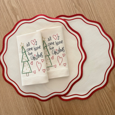 Guardanapos de Natal bordados com textos e corações sobre placemats creme com borda vermelha ondulada