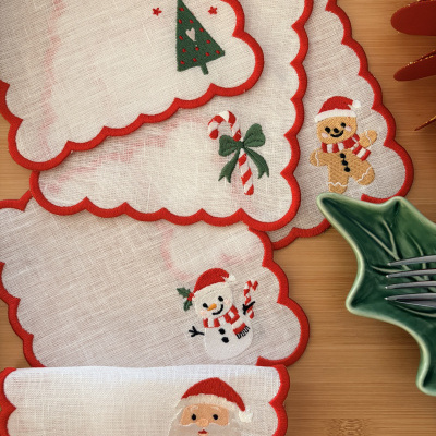 Guardanapos decorativos de Natal com bordados e bordas vermelhas em tecido fino sobre mesa de madeira.