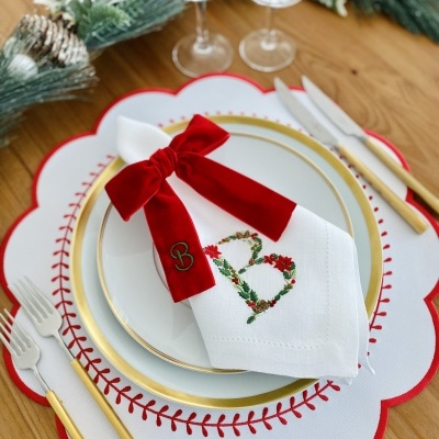 Conjunto de pratos, guardanapo com laço vermelho, talheres dourados e decoração natalícia numa mesa de madeira