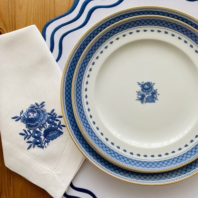Conjunto de pratos de porcelana azul e dourada com guardanapo bordado e caminho de mesa branco com borda azul