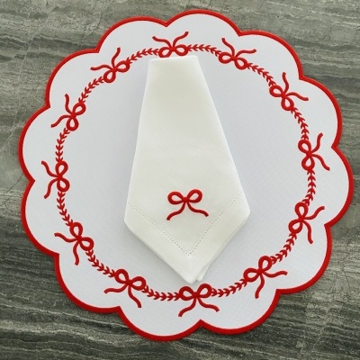 Guardanapo branco bordado com laço vermelho sobre sousplat branco bordado com laços vermelhos