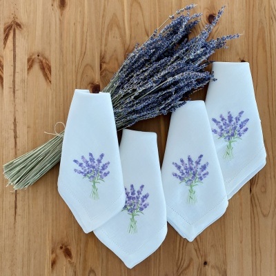 Guardanapos brancos com bordados de lavanda e feixe de lavanda seca numa mesa de madeira