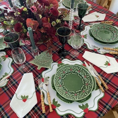 Mesa de jantar decorada para Natal com pratos verdes, toalha tartan vermelha e guardanapos bordados.