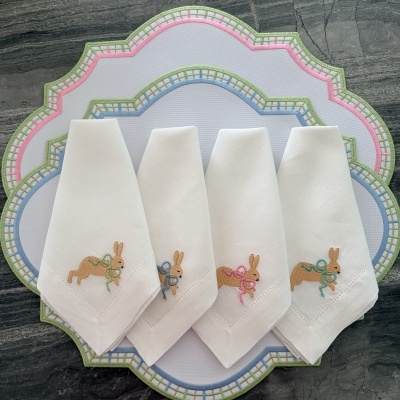 Guardanapos brancos com bordado de coelho e laços coloridos sobre jogos americanos brancos com bordas recortadas e padrão xadrez colorido.