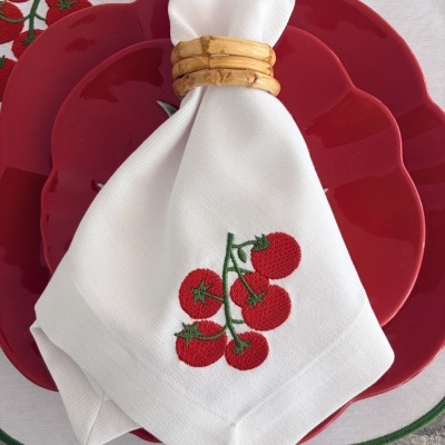 Pratos vermelhos com guardanapo branco bordado com tomates e porta-guardanapo de madeira