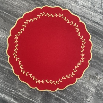 Toalha de mesa vermelha redonda com bordas onduladas e bordado dourado colocada sobre pedra cinzenta