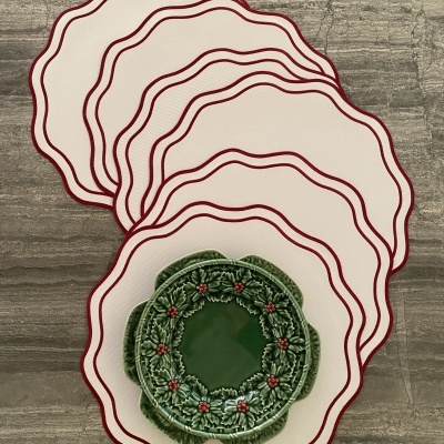 Bases de mesa brancas com borda bordô e prato verde decorativo com folhas e frutos vermelhos.