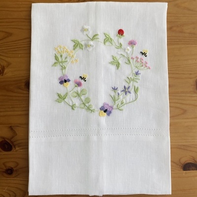 Guardanapo branco com bordado colorido de flores e abelhas sobre mesa de madeira
