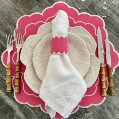 Mesa posta com prato branco, base rosa em forma de flor, guardanapo com argola, talheres com cabo de bambu e copos de vidro