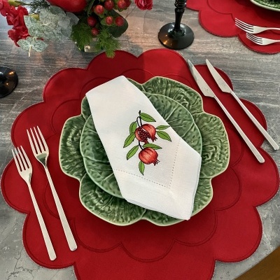Conjunto de loiça verde com pratos em forma de folha, guardanapo bordado, jogos americanos vermelhos ondulados, talheres prateados e copo preto