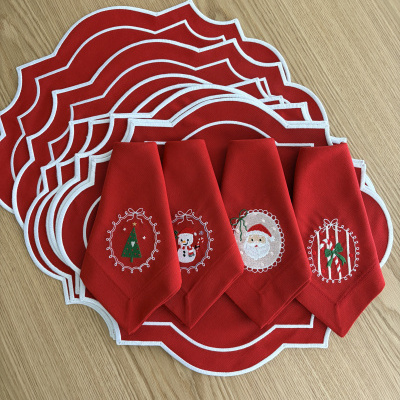 Jogos americanos e guardanapos vermelhos com bordados de Natal em mesa de madeira clara.