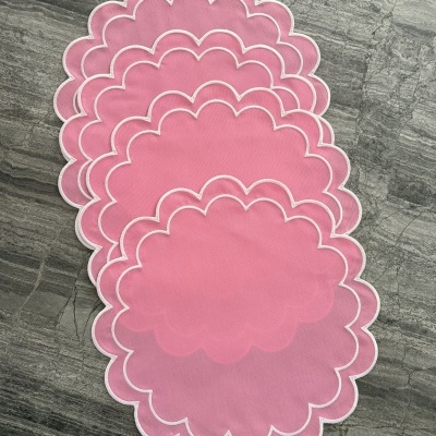 Individuais de mesa cor-de-rosa com borda branca ondulada em superfície de pedra cinza.