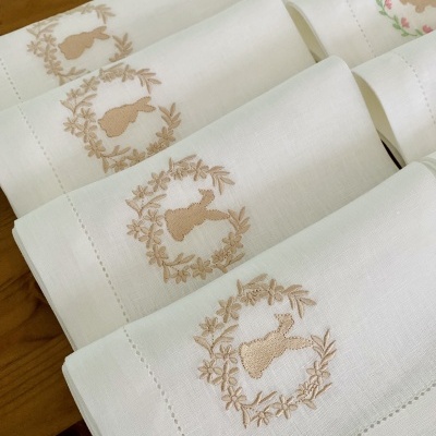 Guardanapos brancos bordados com coelhos bege dobrados sobre madeira