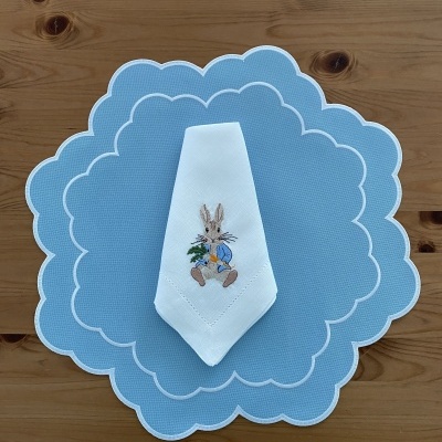 Toalha azul clara com borda branca e guardanapo branco com bordado de coelho