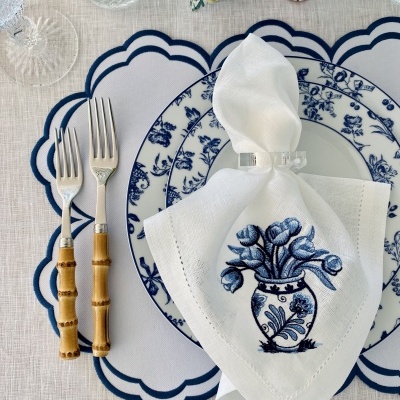 Mesa posta com prato branco e azul, talheres com cabos de bambu, guardanapo branco bordado e copos de vidro