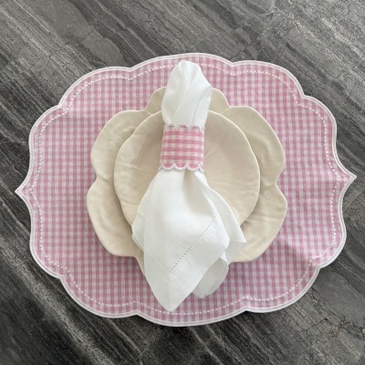 Jogo de mesa com pratos cerâmicos creme, guardanapo branco com argola xadrez rosa e branco, individual têxtil rosa xadrez em superfície cinzenta