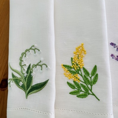 Três guardanapos brancos com bordados florais coloridos