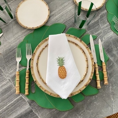 Conjunto de louça e talheres com padrão de bambu e acessório decorativo de ananás numa mesa cinza.