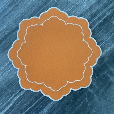 Guardanapos decorativos laranja em forma de flor com bordas brancas sobre superfície de pedra cinza-azulada