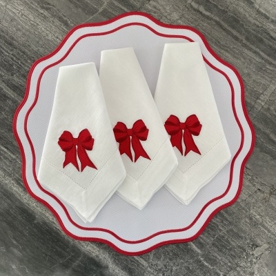 Três guardanapos brancos com laços vermelhos sobre base branca com borda vermelha