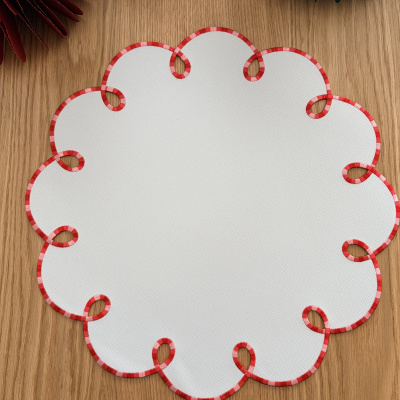 Toalha redonda branca com bordas onduladas em tecido vermelho e branco sobre mesa de madeira