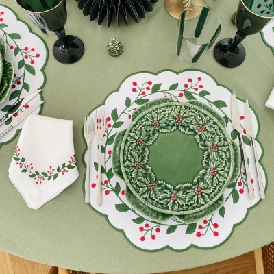 Jantar de Natal com pratos e copos decorativos em verde e vermelho sobre mesa com toalha verde claro