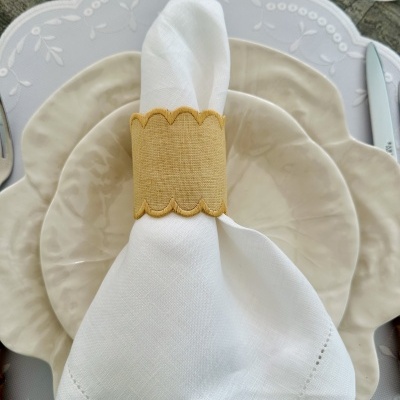 Conjunto de pratos de cerâmica bege com guardanapo branco e argola amarela em mesa de madeira.