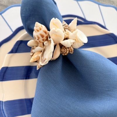 Guardanapo azul com anel de conchas sobre prato branco e azul.