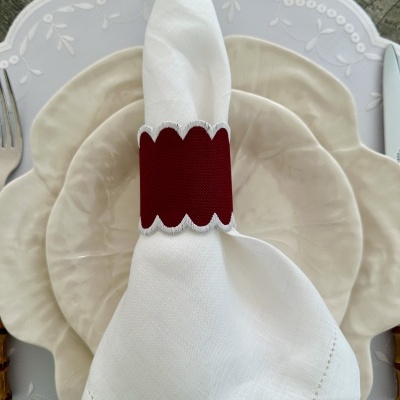 Guardanapo branco com anel de guardanapo vermelho e pratos bege.