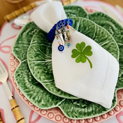 Conjunto de pratos verdes formato folha com guardanapo branco e anel decorativo azul sobre mesa arrumada.