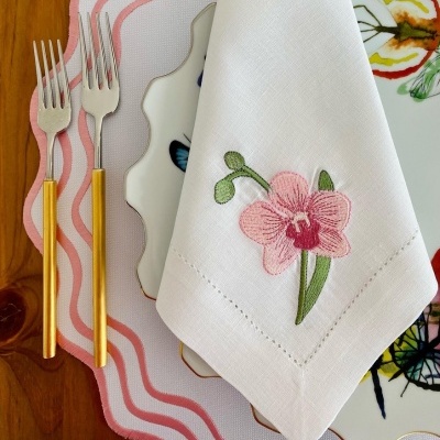 Guardanapo branco com bordado rosa sobre prato com borboletas, jogo americano rosa, garfos com cabo amarelo