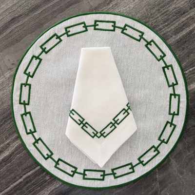 Jogo americano e guardanapo branco com bordado verde geométrico.