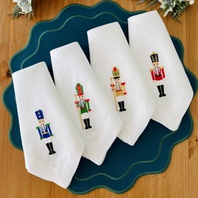 Quatro guardanapos brancos bordados com soldados quebra-nozes sobre apoio de mesa azul escuro e decoração natalícia