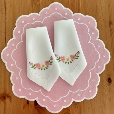 Toalhetes bordados florais sobre apoio rosa em mesa de madeira