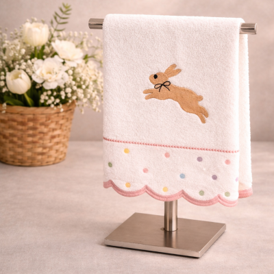 Toalha branca com bordado de coelho e bolinhas coloridas pendurada em suporte metálico