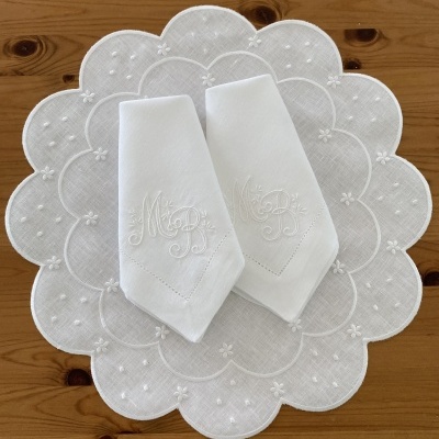 Toalhetes brancos bordados sobre toalhete redondo decorativo branco numa mesa de madeira