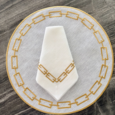 Conjunto de mesa branco com bordado amarelo mostarda sobre superfície de mármore cinza