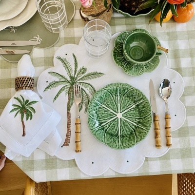 Mesa posta com prato, chávena e talheres com tema de folhas e palmeira, e arranjo floral