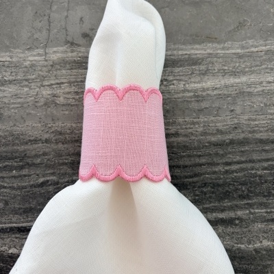 Guardanapo branco com argola rosa bordada sobre superfície cinza