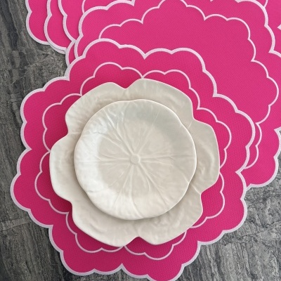Três pratos brancos em forma de flor sobre descanso de pratos rosa em superfície de pedra.