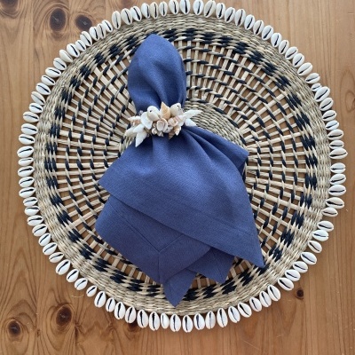 Guardanapo azul com anel de conchas sobre base de palha circular bordada com búzios