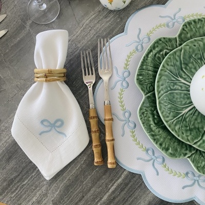 Mesa posta com guardanapo branco, garfos com cabo de bambu, prato verde em forma de folha, base branca com pattern azul, ovo decorativo e copo de vinho